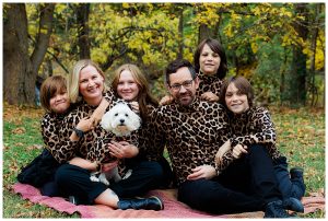 Family of six plus a small white dog all wear matching leopard print.