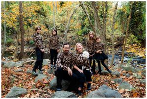 Family wearing matching leopard outfits poses in forest setting