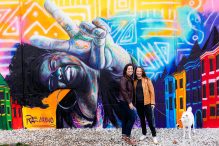 LGBTQ couple poses with their dog against a colorful mural for their Eckington DC engagement photography session.