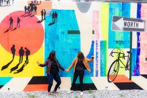 LGBTQ couple does a fun dance move against a colorful city bike mural for their Eckington DC engagement photography session.