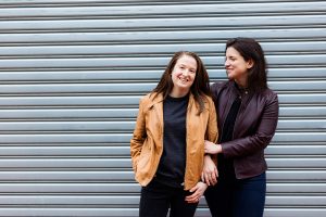 LGBTQ couple snuggles in front of a chrome garage door for their urban Eckington DC engagement photography session.