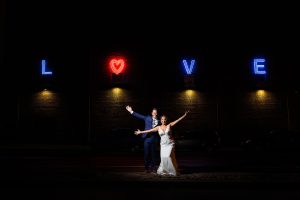 Bride and groom pose for an outdoor night shot in front of the love sign at the American Visionary Art Museum in Baltimore.