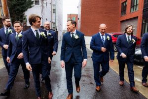 Groom and groomsmen walk to the church on a rainy spring day.