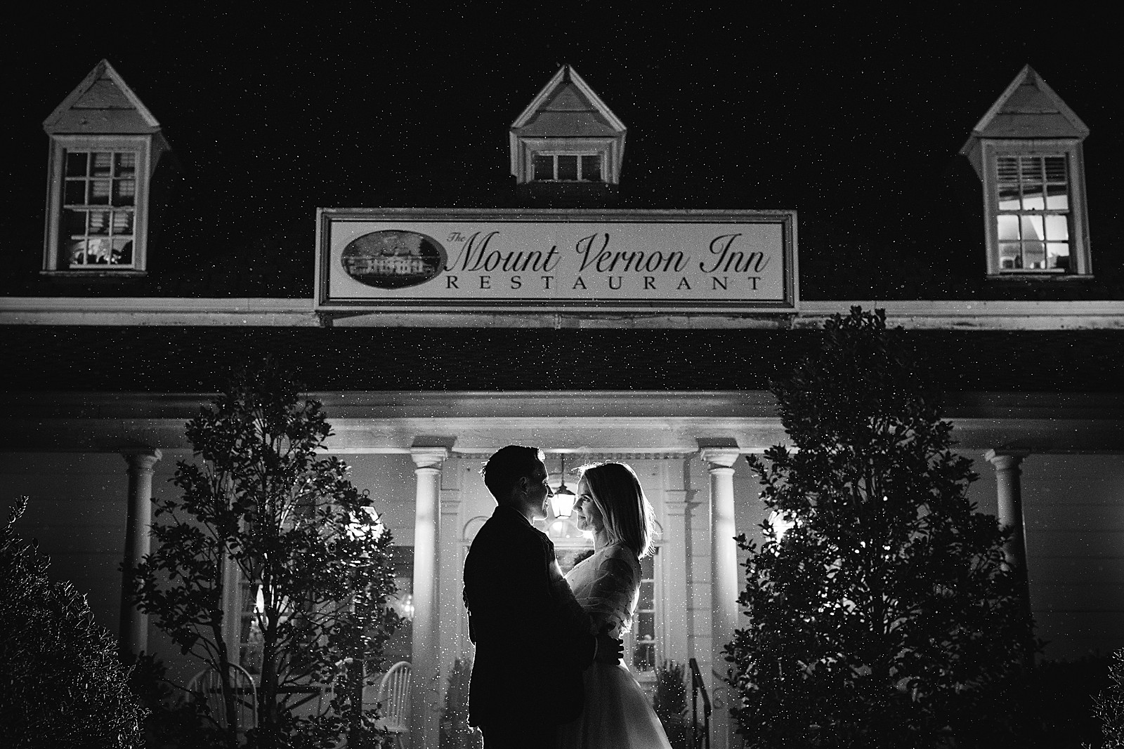 Bride and groom stand in front of the front of the Mount Vernon Inn Restaurant in a misty rain at night.