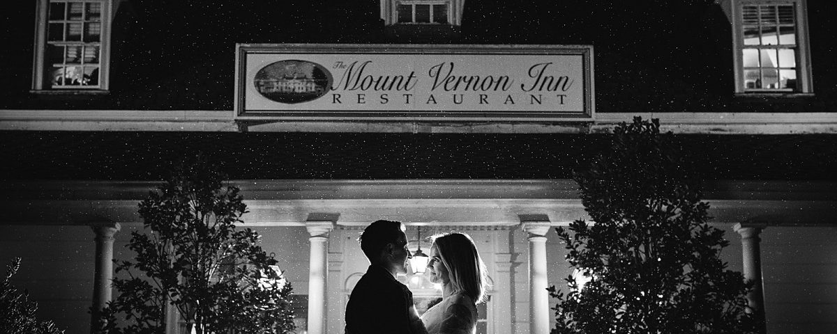 Bride and groom stand in front of the front of the Mount Vernon Inn Restaurant in a misty rain at night.