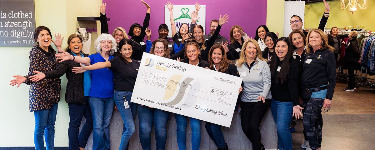 A group of Sandy Spring Bank volunteers smiles at the camera and poses with donation check for Women Giving Back.