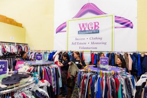 Wide shot of four people going through multiple racks of clothing at a corporate volunteer event at Women Giving Back.