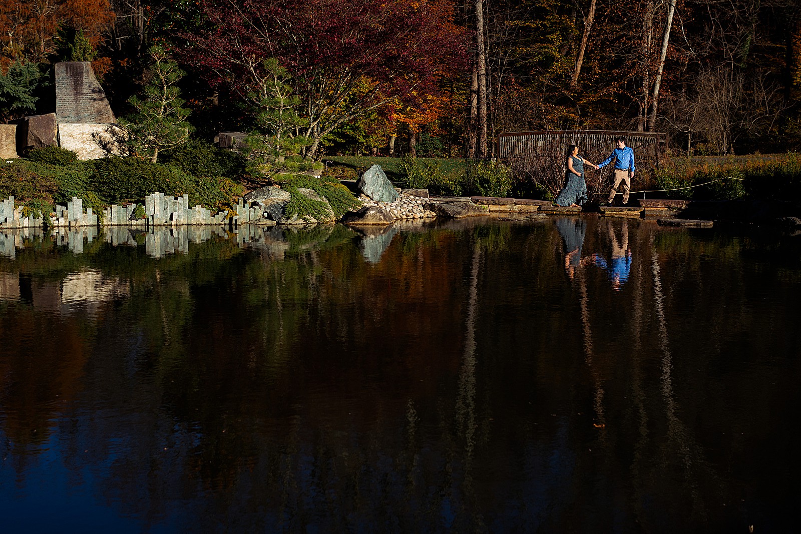 A couple walks across a path on a lake holding hands.