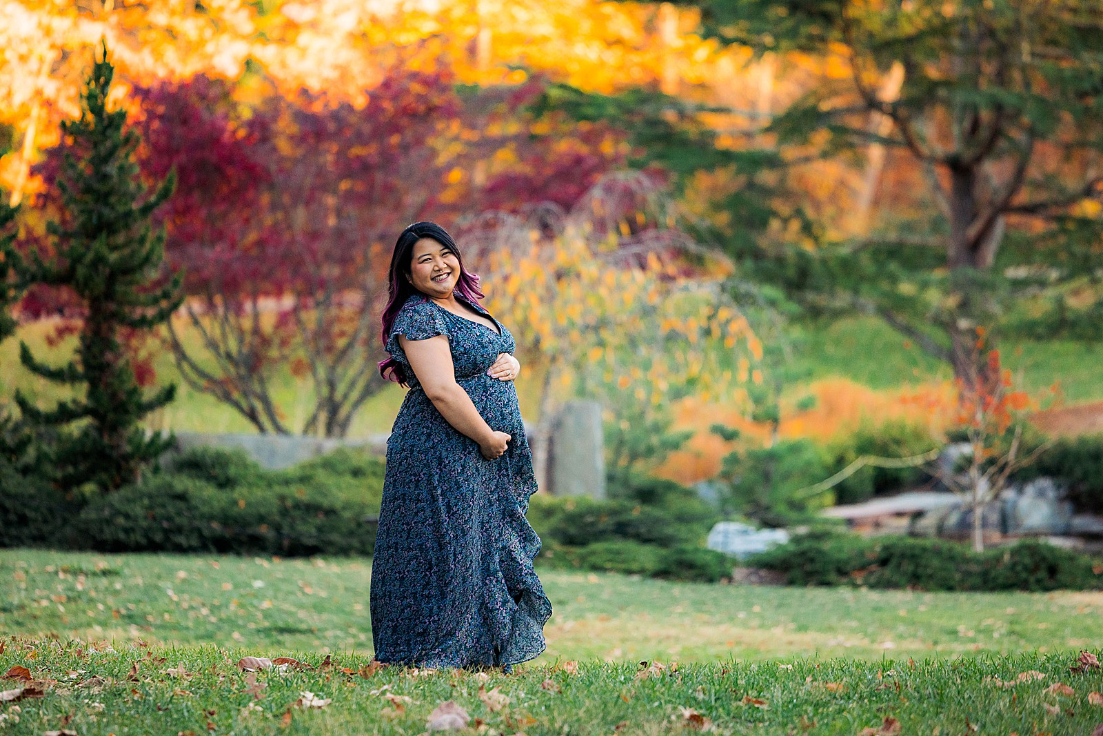 A pregnant woman holds her belly at her fall Brookside Gardens maternity session.