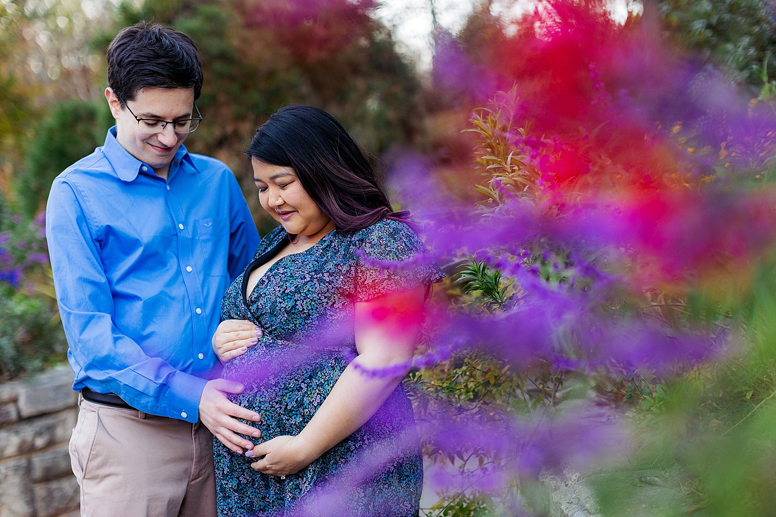 A couple looks down while holding a pregnant belly at a maternity session at Brookside Gardens.