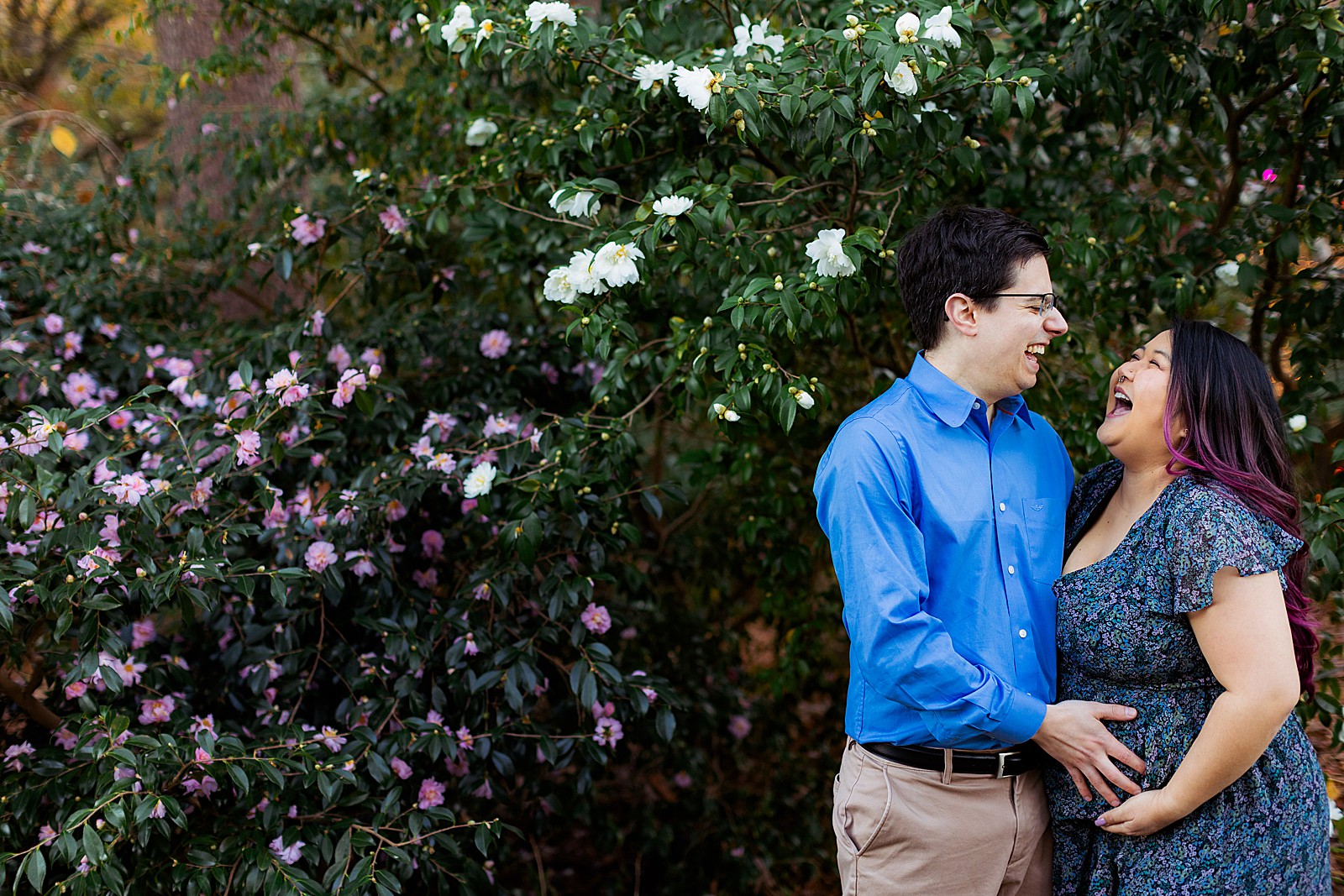 A couple laughs together while looking down at a maternity belly.