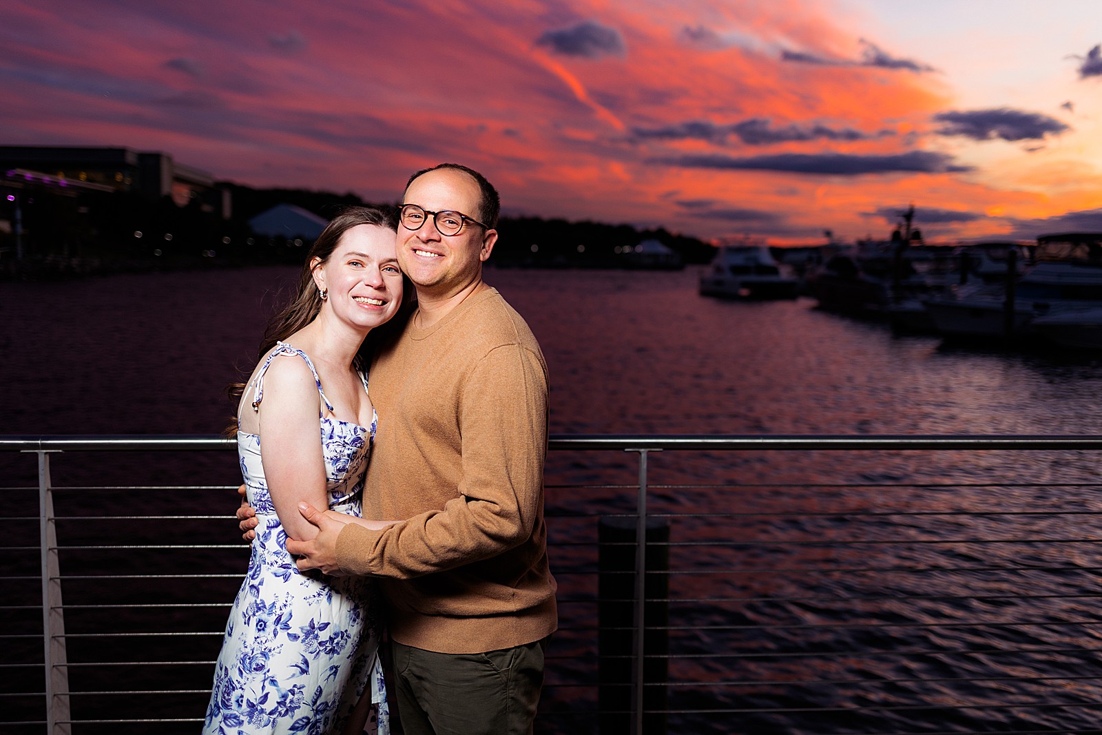 A couple smiles at the camera during their sunset engagement photo session at the National Harbor. 