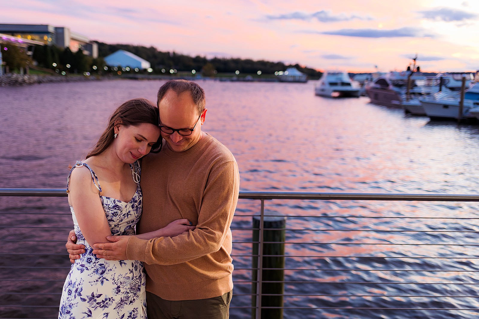 A couple hugs in front of the water at the National Harbor during their sunset engagement session. 