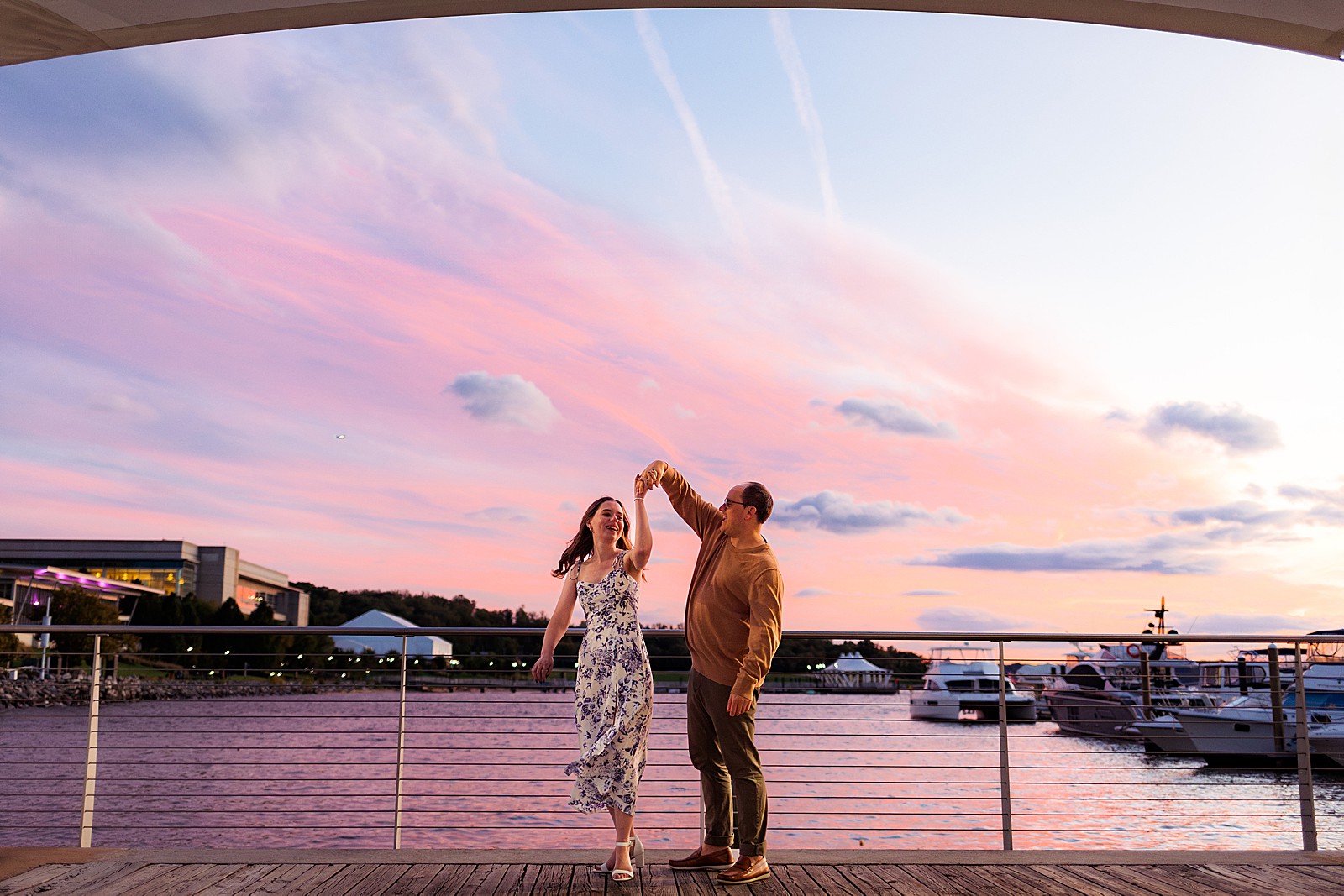 A couple twirls in front of the National Harbor during their beautiful sunset engagement session. 