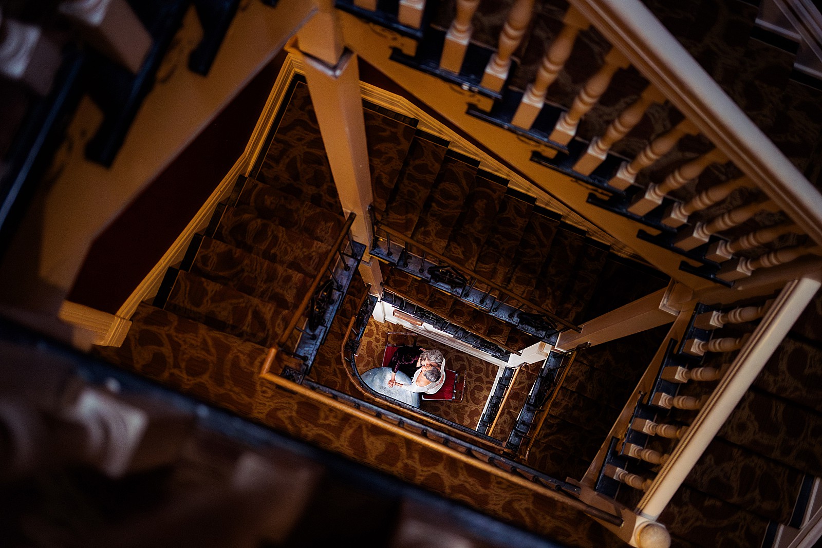 A couple leans in at the bottom of the staircase at the Tabard Inn while the camera looks down.